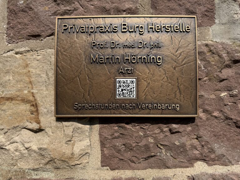 Bronzeschild der Privatpraxis Burg Herstelle mit dem Namen Prof. Dr. med. Dr. phil. Martin Hörning an der Sandsteinmauer