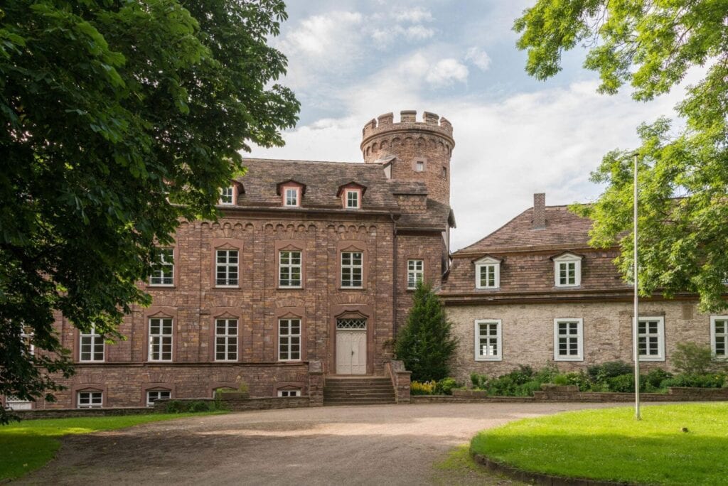 Die Burg Herstelle von der Zufahrt aus gesehen: das Herrenhaus aus rotem Sandstein mit dem Rundturm, rechts der Wirtschaftsflügel